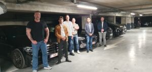 Illustration photoréaliste montrant des chauffeurs VIP en formation dans le parking de France Limousine Service, entourés de limousines, vans et minibus de luxe. Les chauffeurs, en tenue civile, ont suivi un exercice de conduite sécurisée. Ambiance professionnelle et luxueuse, éclairage naturel, style moderne et détaillé. (Tous Droits réservés SF3Pro)